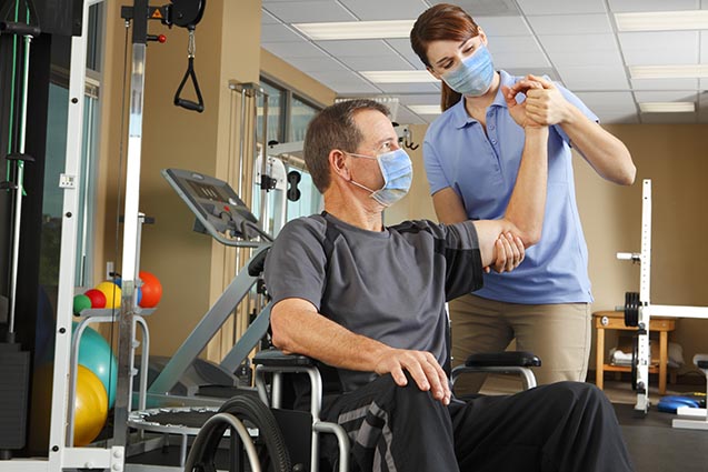 Man in wheelchair receiving rehabilitation assistance from therapist in blue shirt